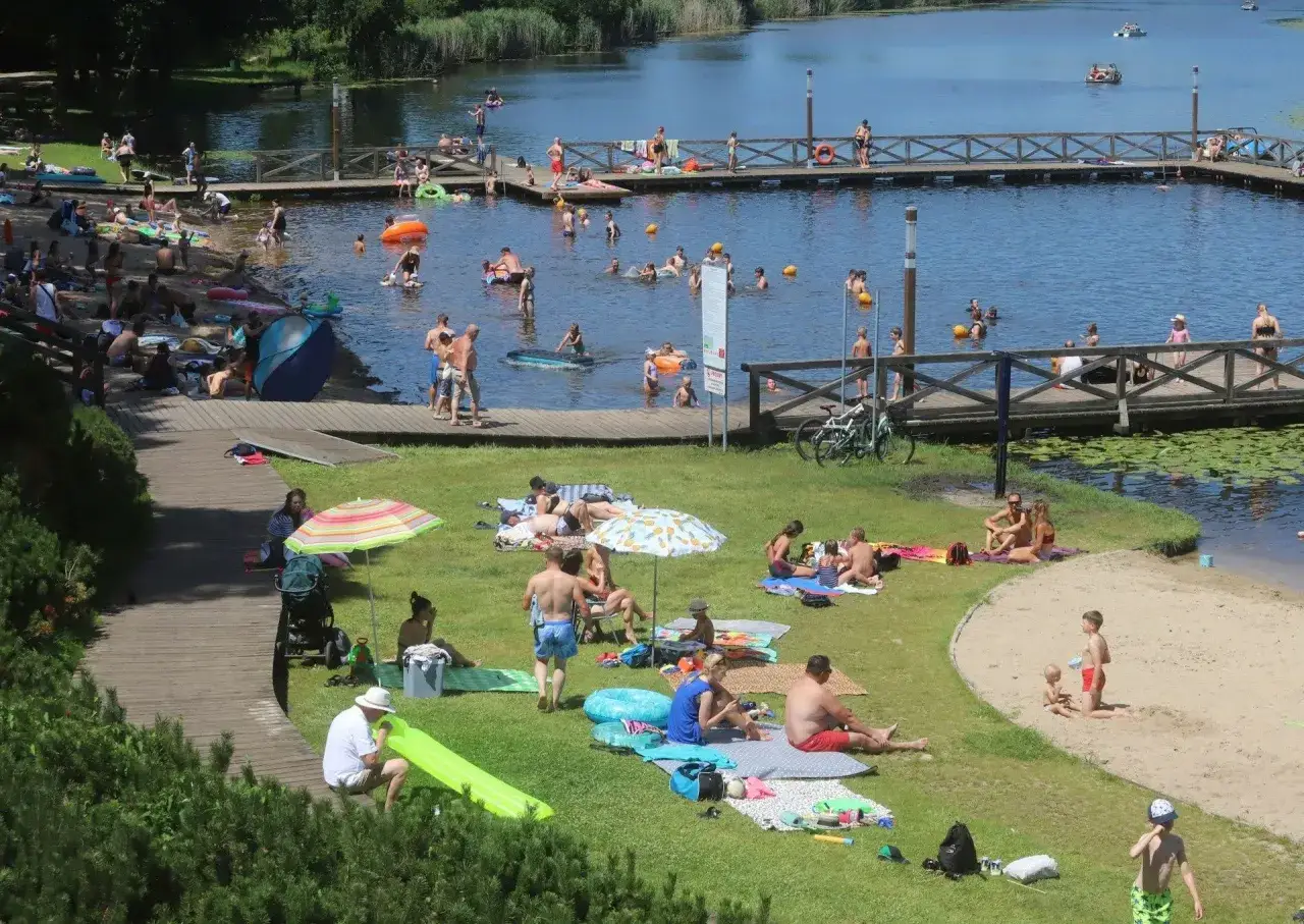 Ludzie odpoczywają i kąpią się nad jeziorem Kozienickim. Słoneczny dzień zachęca do relaksu na plaży i w wodzie.