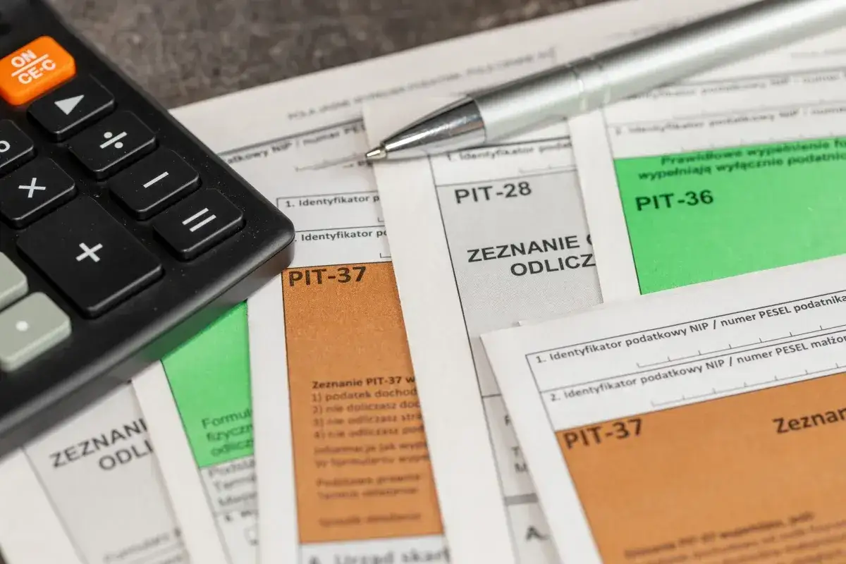 Kalkulator i długopis na dokumentach PIT-37, PIT-28, PIT-36. Czas rozliczyć podatki, może nawet uda się uzyskać 1000 plus!