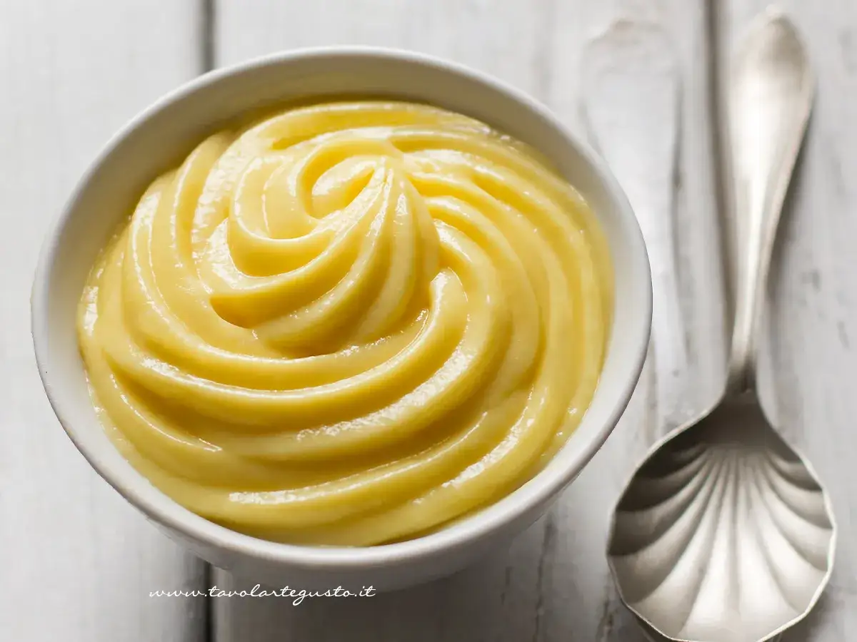 Una ciotola bianca piena di soffice crema chantilly, con una cucchiaio d'argento accanto.