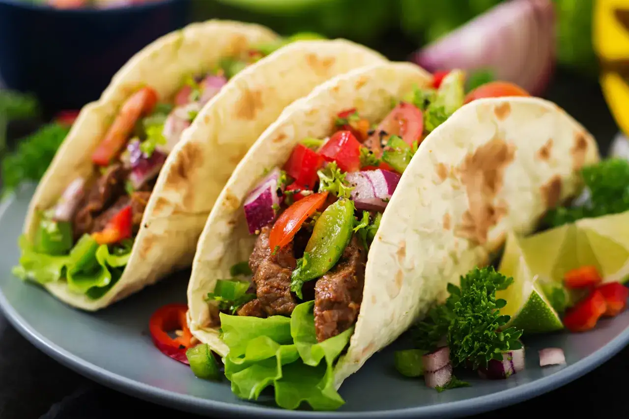 Pyszne tacos z mięsem, sałatą, pomidorami i czerwoną cebulą. Idealny przepis na tacos dla każdego.