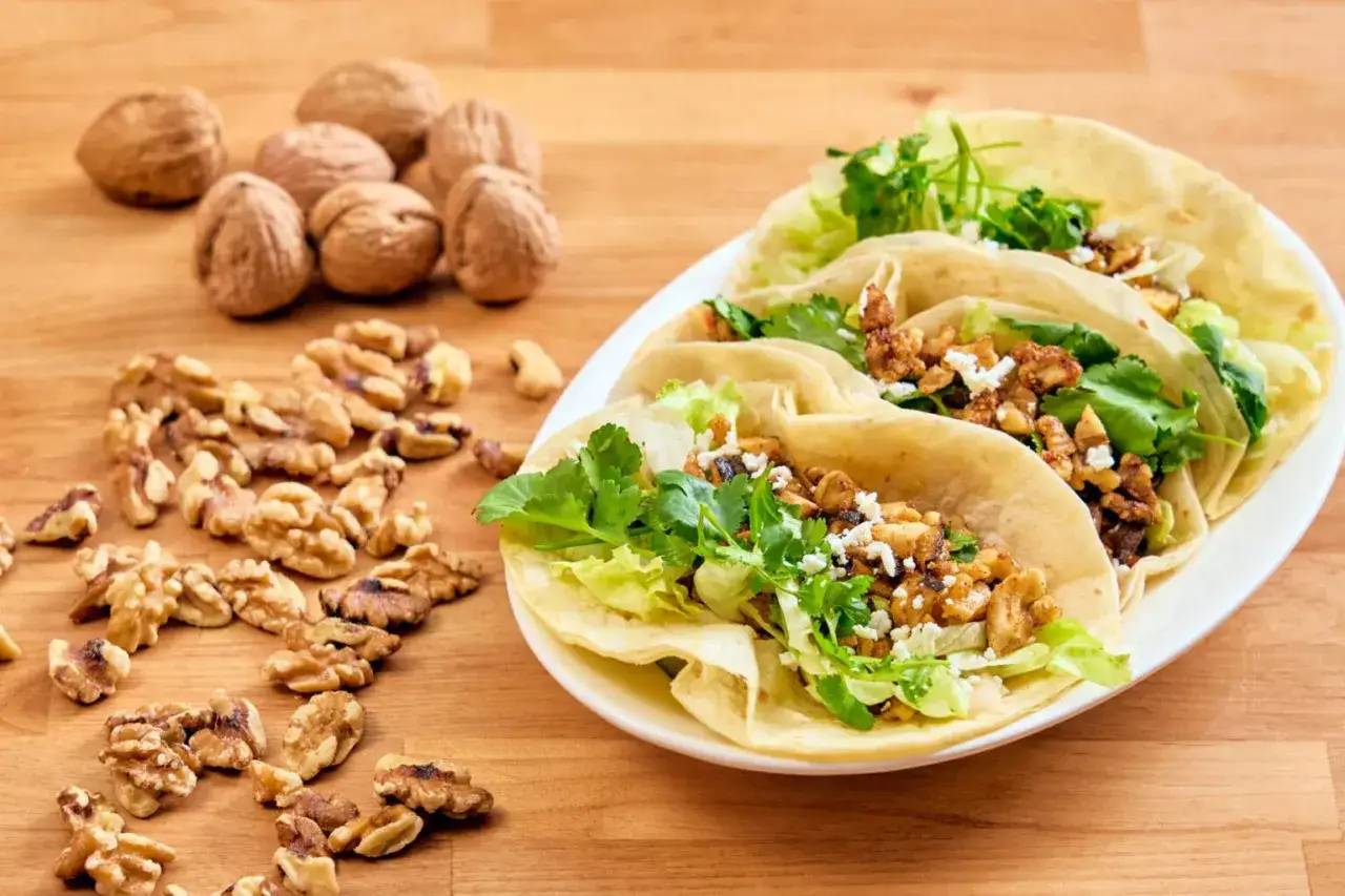 Deliciosos tacos vegetarianos rellenos de nueces, lechuga y cilantro fresco, acompañados de nueces enteras y partidas.