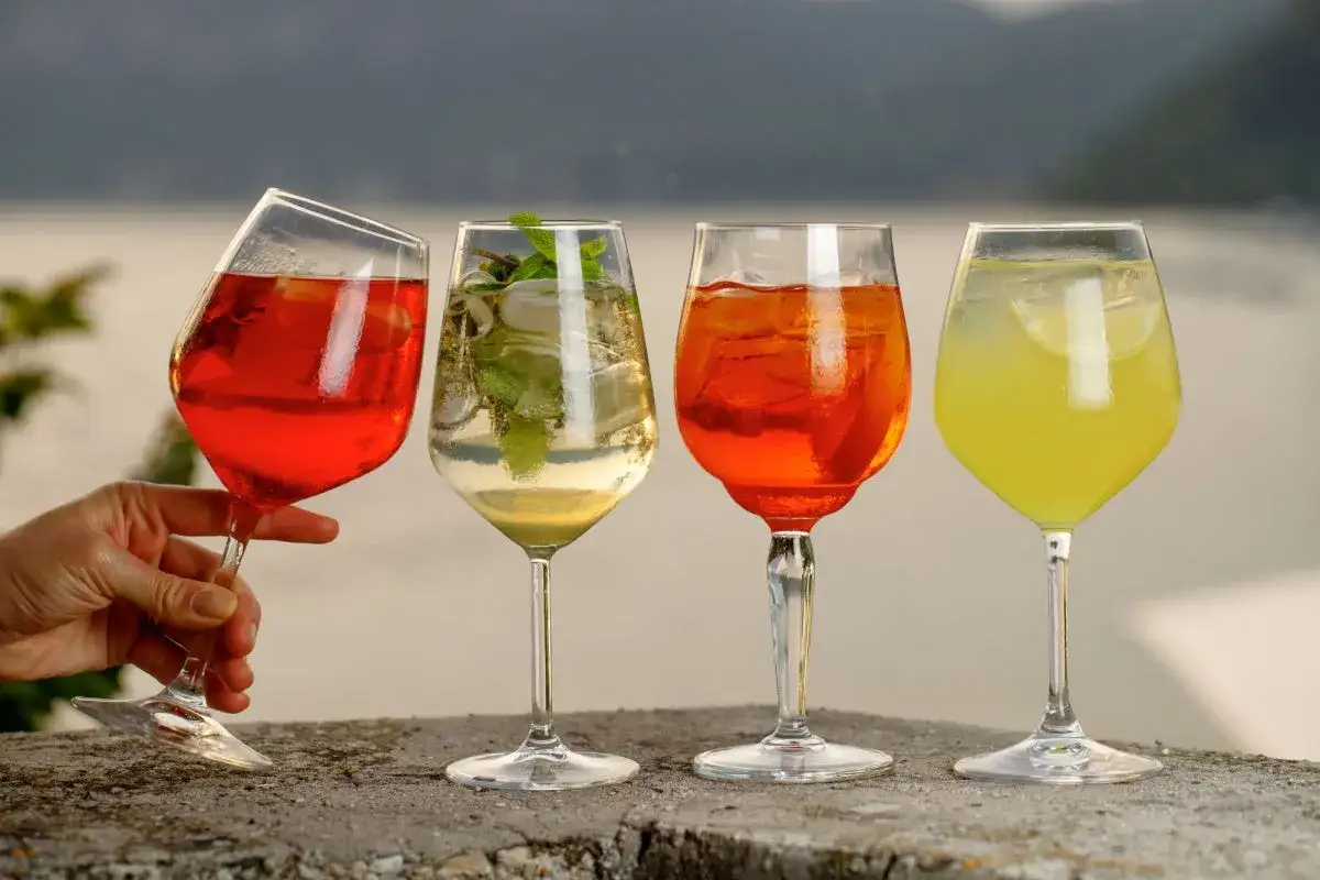 Vier Gläser mit Aperol Spritz Varianten, darunter ein roter, ein heller mit Minze, ein klassischer Aperol und ein gelber Drink.