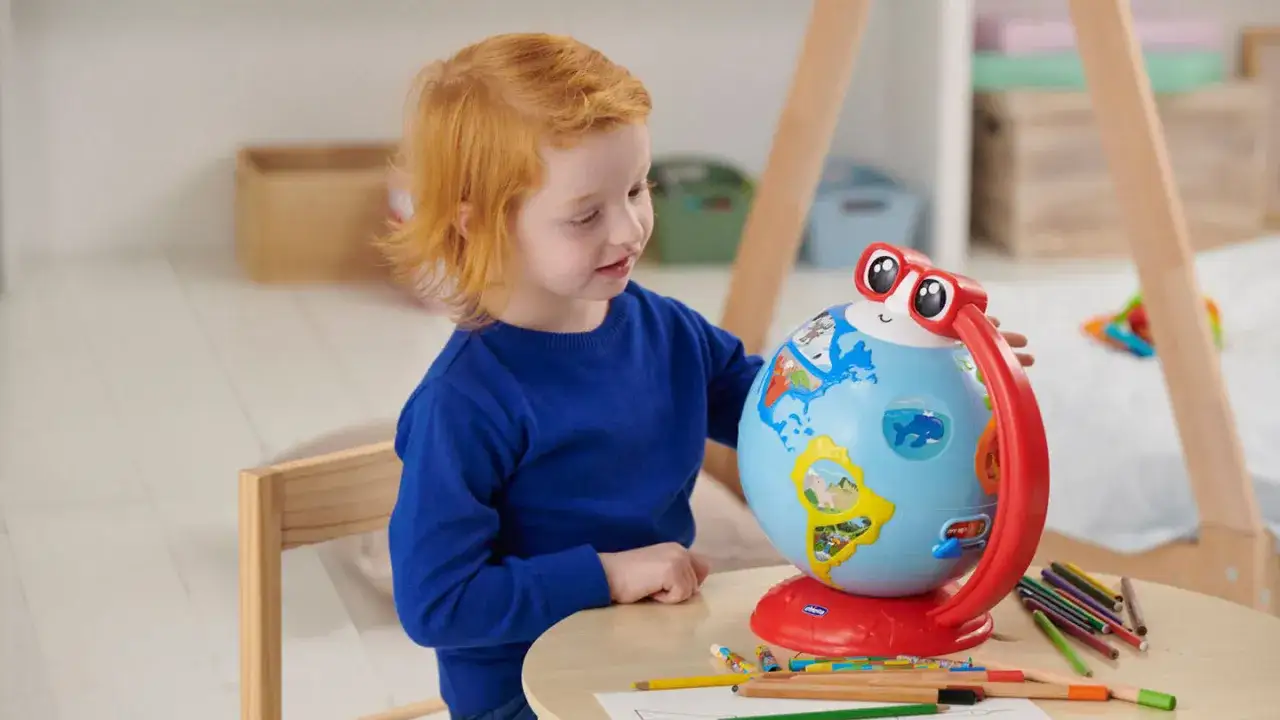Bambino con capelli rossi esplora un globo interattivo, un esempio di bambini plusdotati 2 anni che imparano divertendosi.
