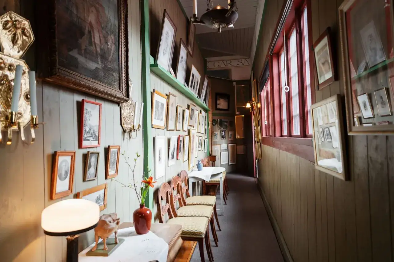 En korridor fylld med konst, som p&aring;minner om Carl Larssons hem. Tavlor och ljusstakar pryder v&auml;ggarna.