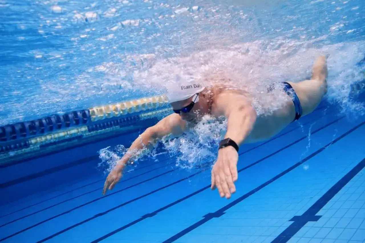 Swimmer performing butterfly stroke sets, creating a powerful splash as they glide through the blue water.
