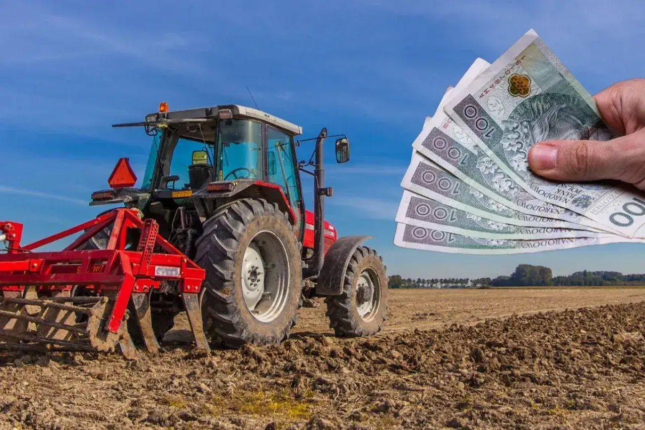 Czerwony traktor na polu, ręka pokazuje banknoty 100 zł. Czy rolnicy płacą podatek od nieruchomości?