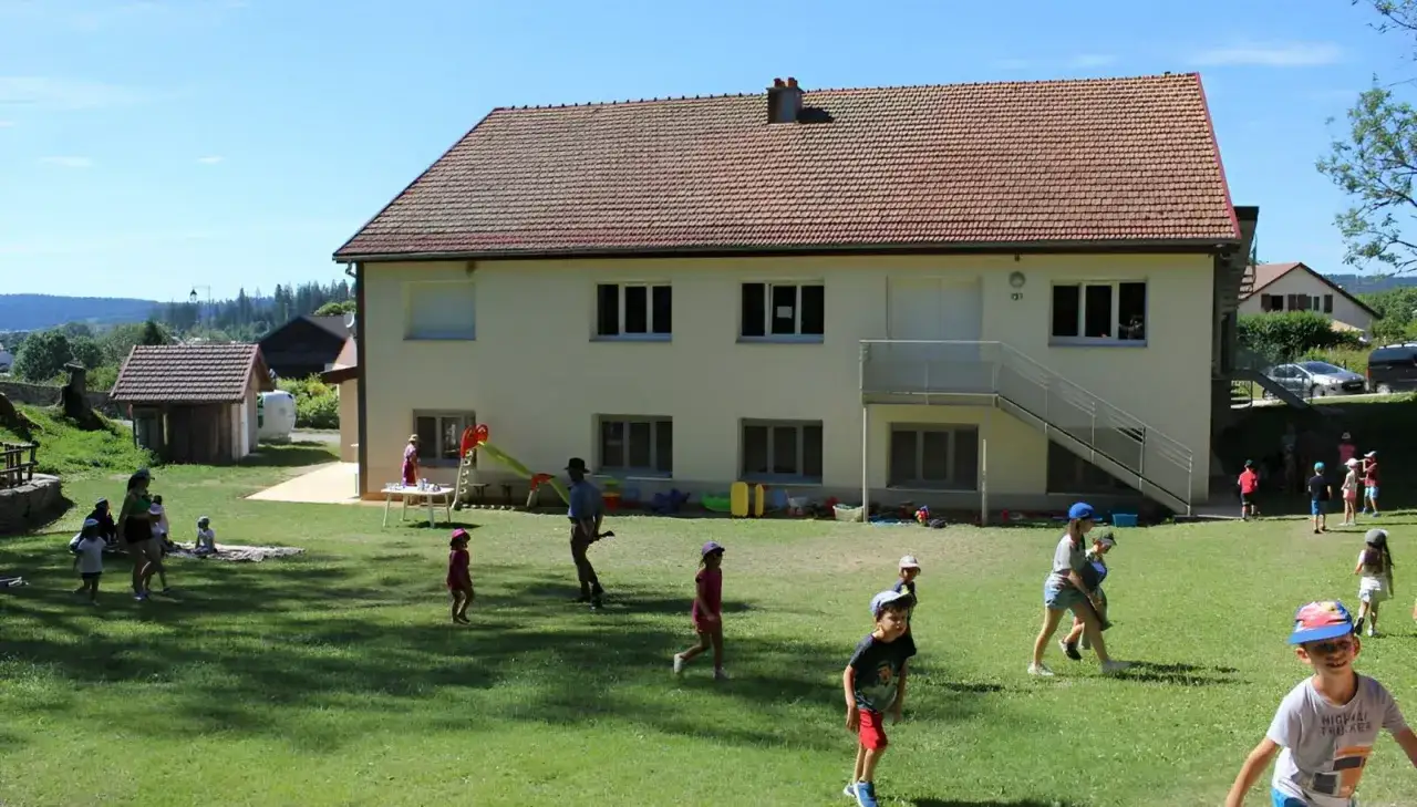 Enfants jouant dans la cour d'une colonie de vacances en Moselle. Le soleil brille sur l'herbe verte.