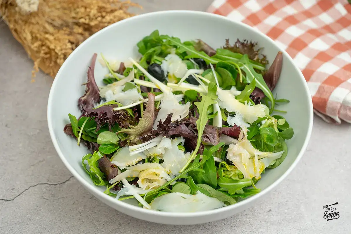 Deliciosa ensalada de bacalao con hojas verdes, aceitunas negras y lascas de queso. Un plato fresco y lleno de sabor.