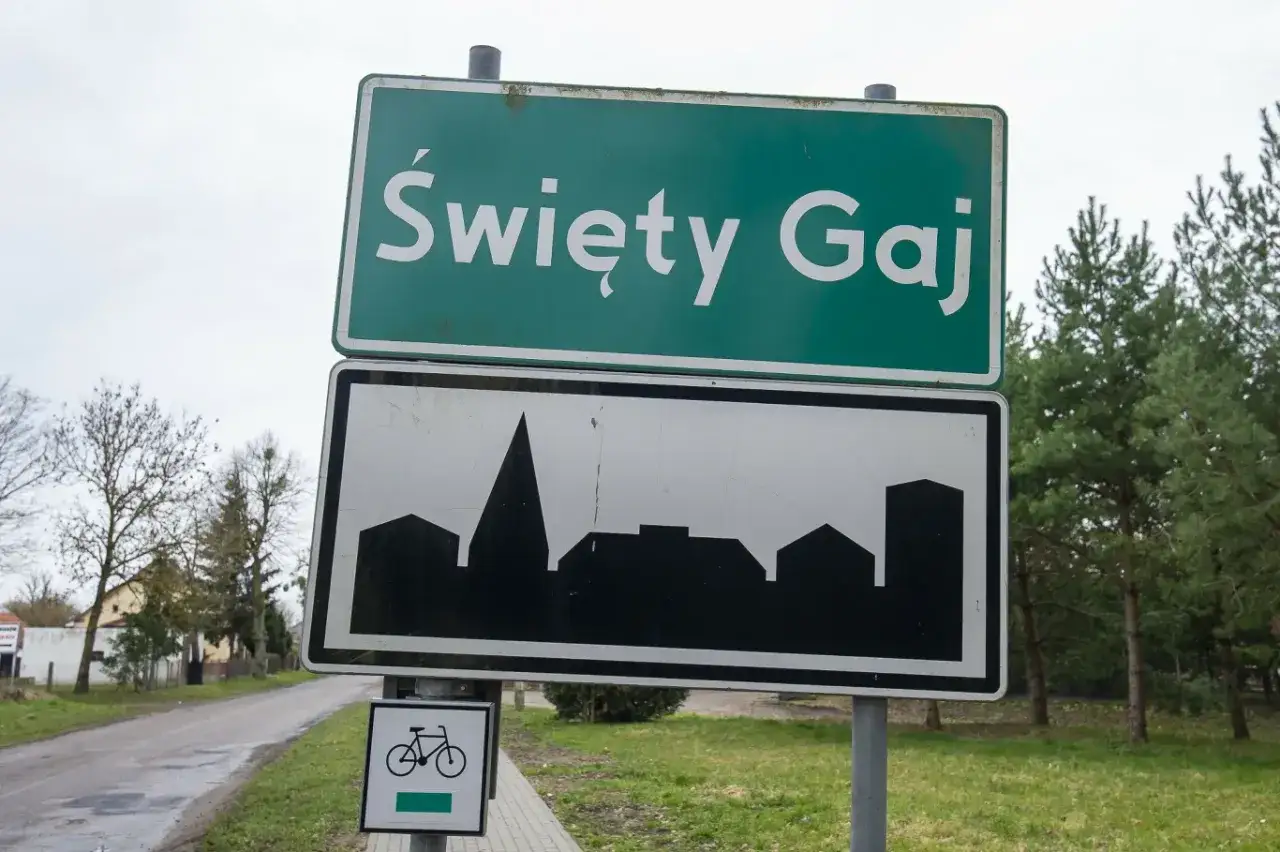Zielony znak miejscowości Święty Gaj z sylwetką zabudowań i symbolem roweru.