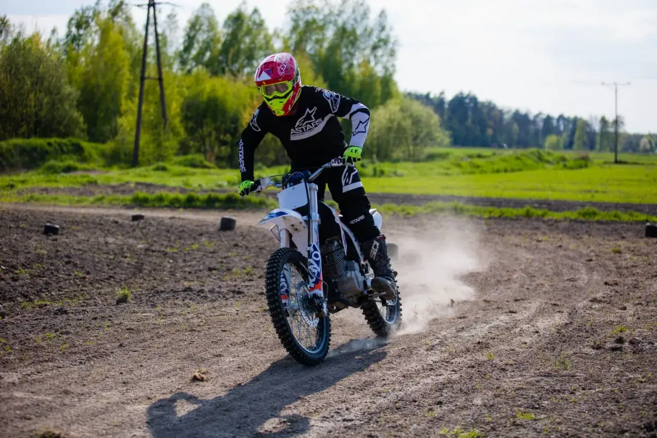 Motocrossowiec w kasku i goglach śmiga po piaszczystym torze, wzbijając tumany kurzu. Idealne miejsce, gdzie można jeździć crossem.