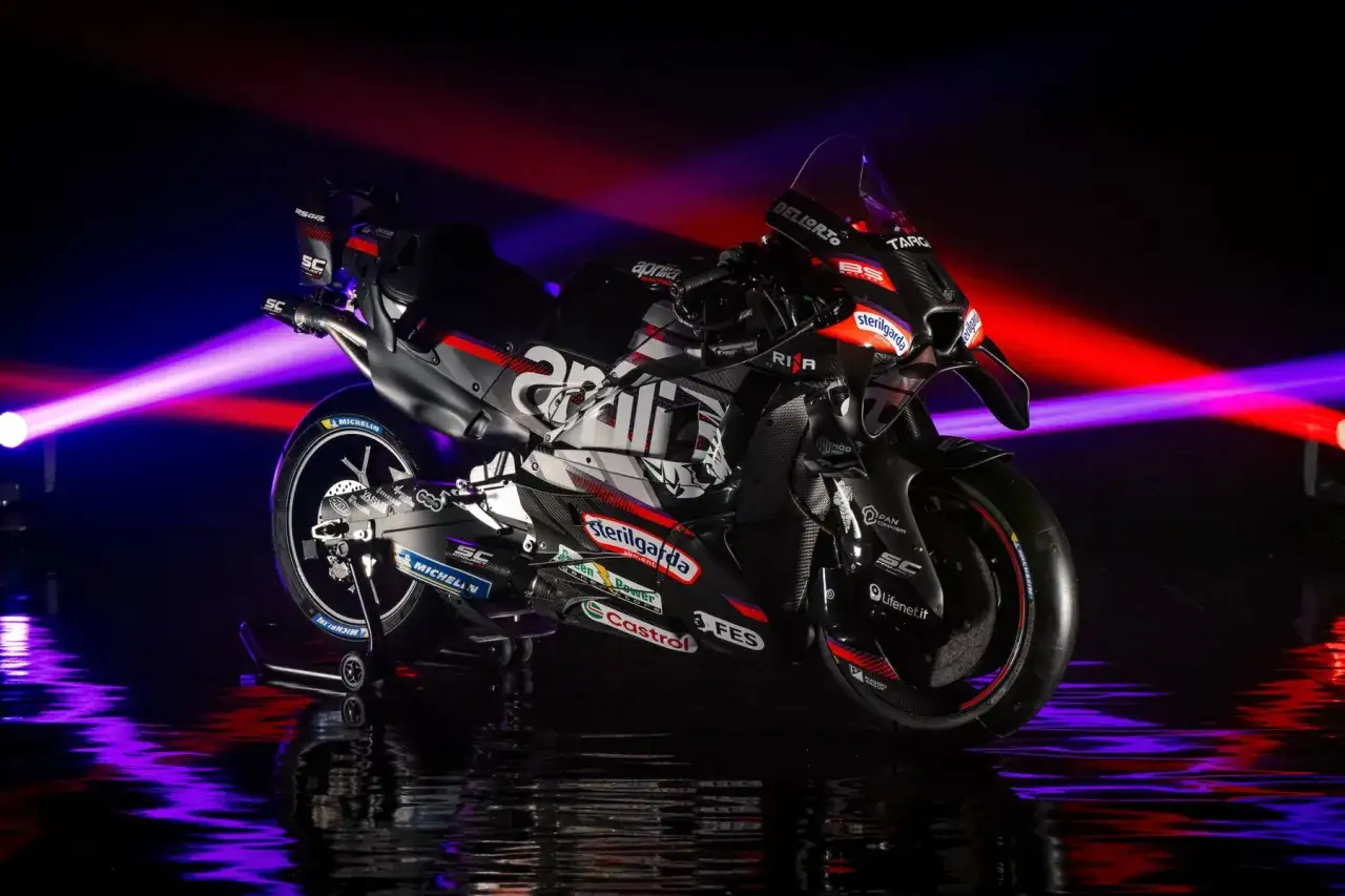 La Aprilia MotoGP lista para la carrera, con luces rojas y púrpuras iluminando su diseño agresivo y patrocinadores.