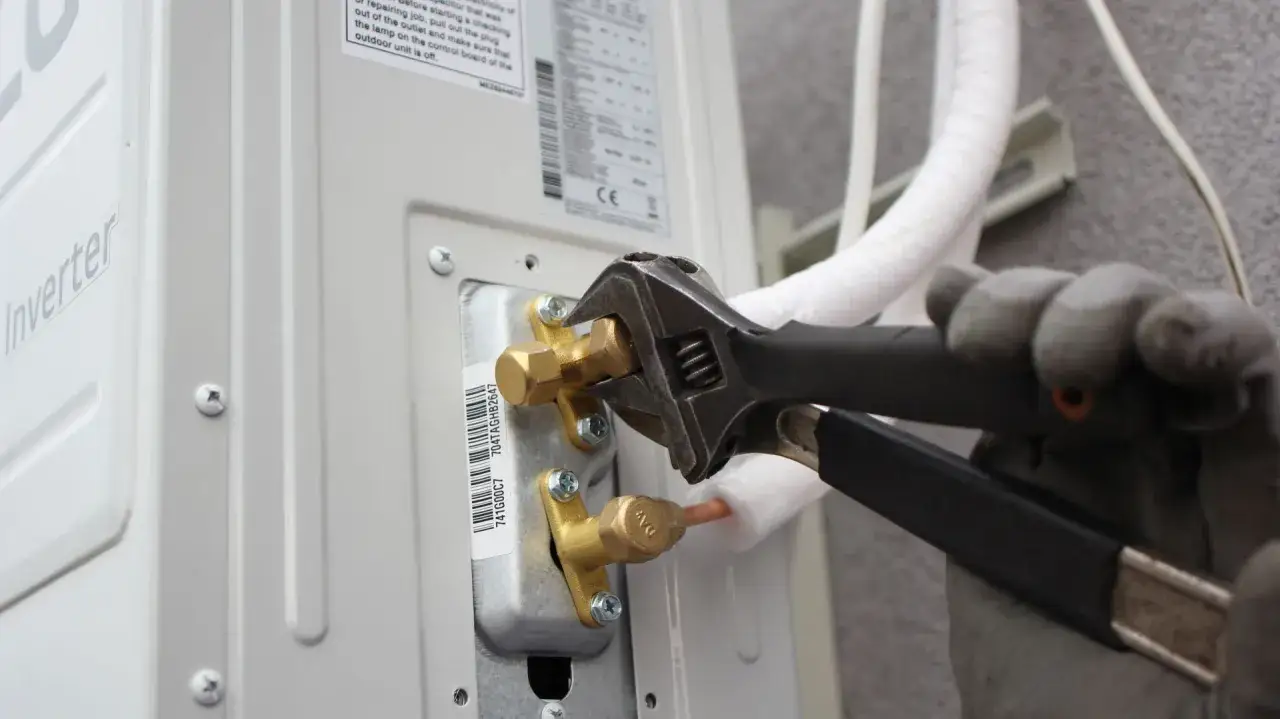Instalator dokręca kluczem zawór przy jednostce klimatyzacyjnej.