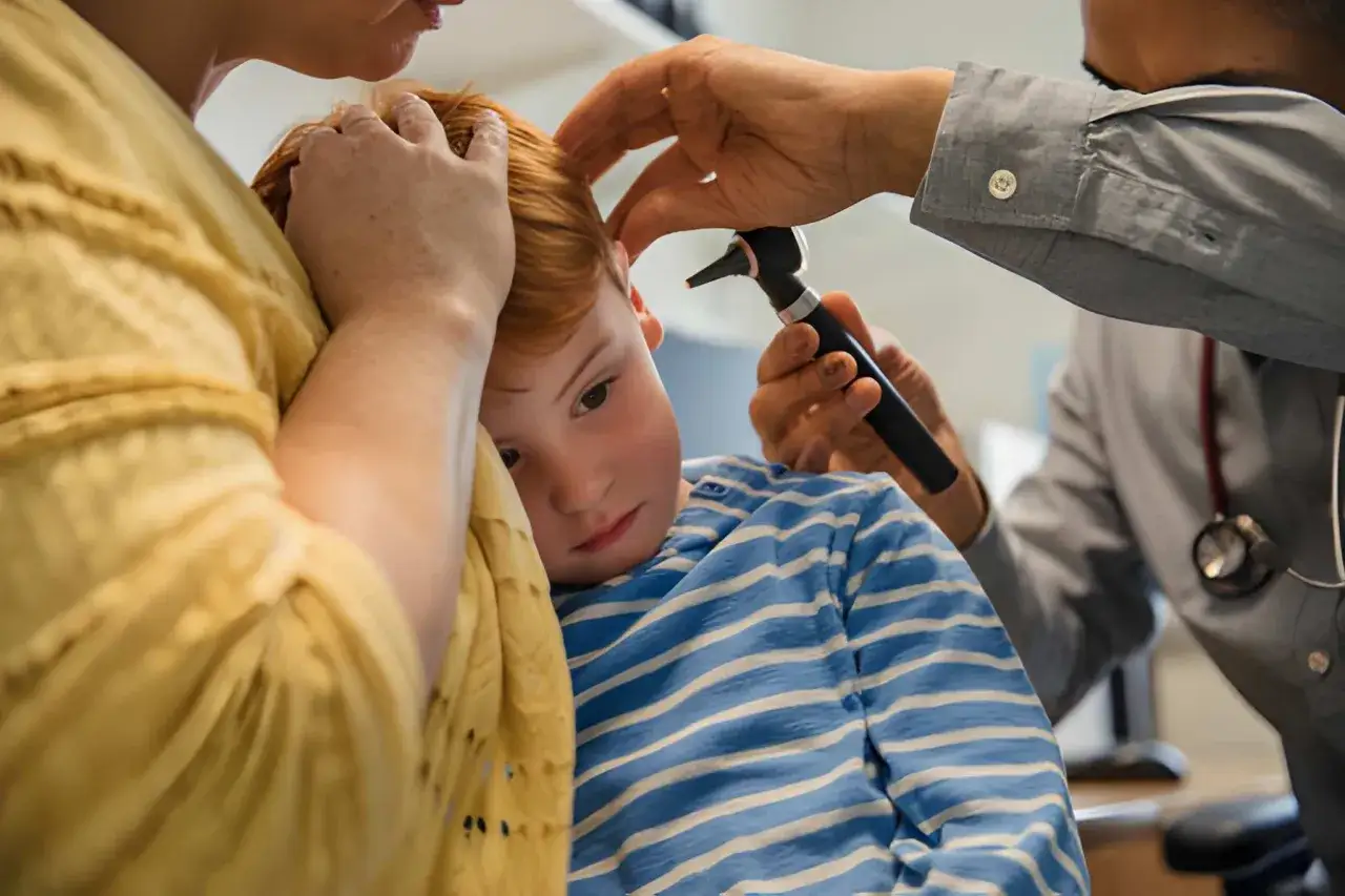Ni&ntilde;o con dolor de o&iacute;do es examinado por un doctor. La madre lo abraza.