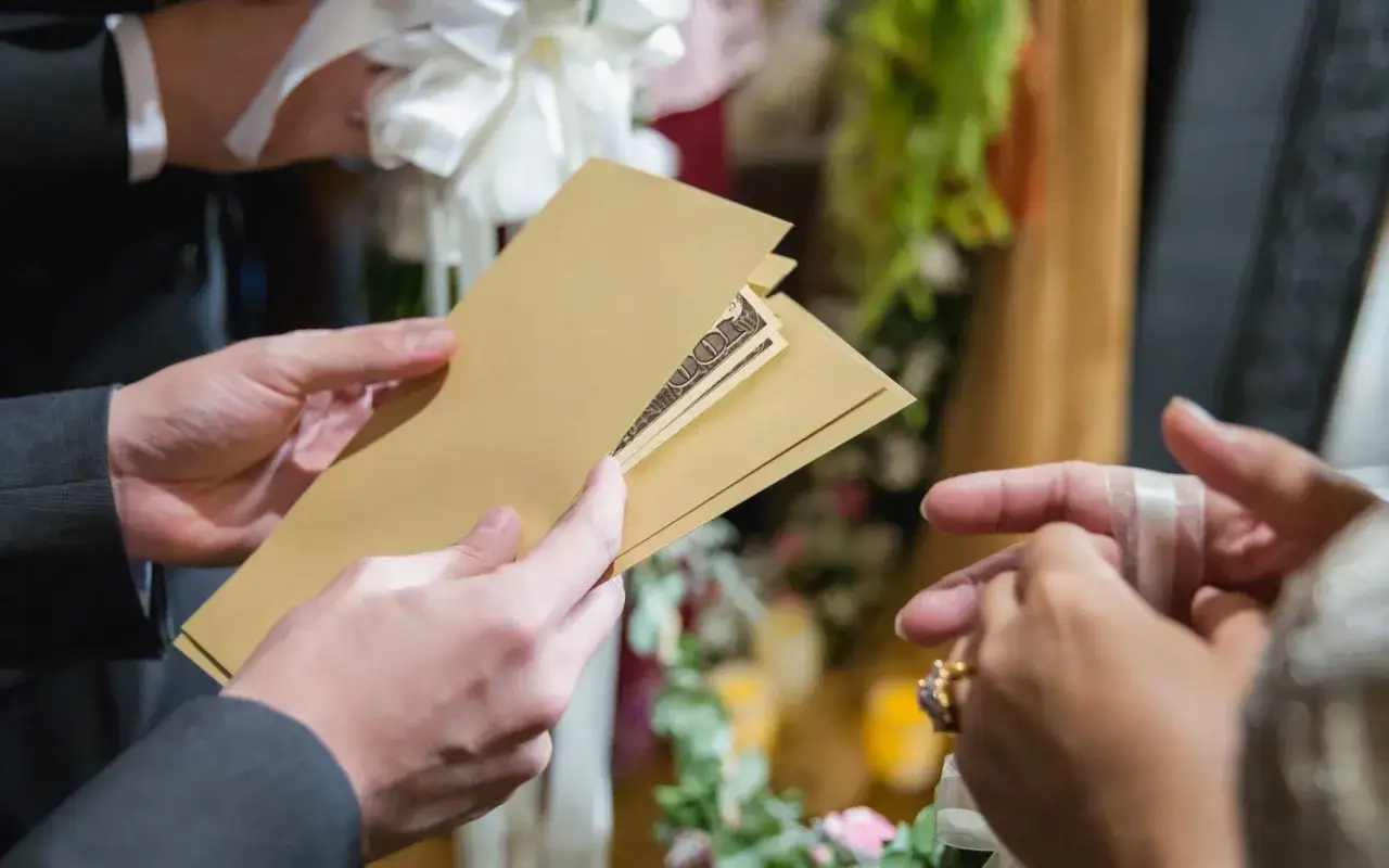 Une main tend une enveloppe dor&eacute;e contenant des billets, un cadeau de mariage, &agrave; une autre main orn&eacute;e d'une bague.
