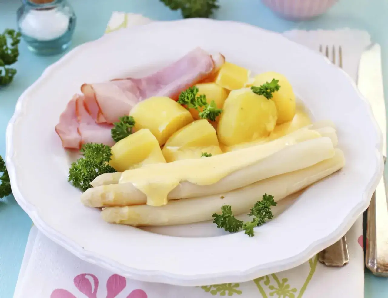 Ein Teller mit weißem Spargel, Kartoffeln, Schinken und Sauce Hollandaise. Ein klassisches Gericht, das zu den beliebtesten Spargel Rezepten zählt.