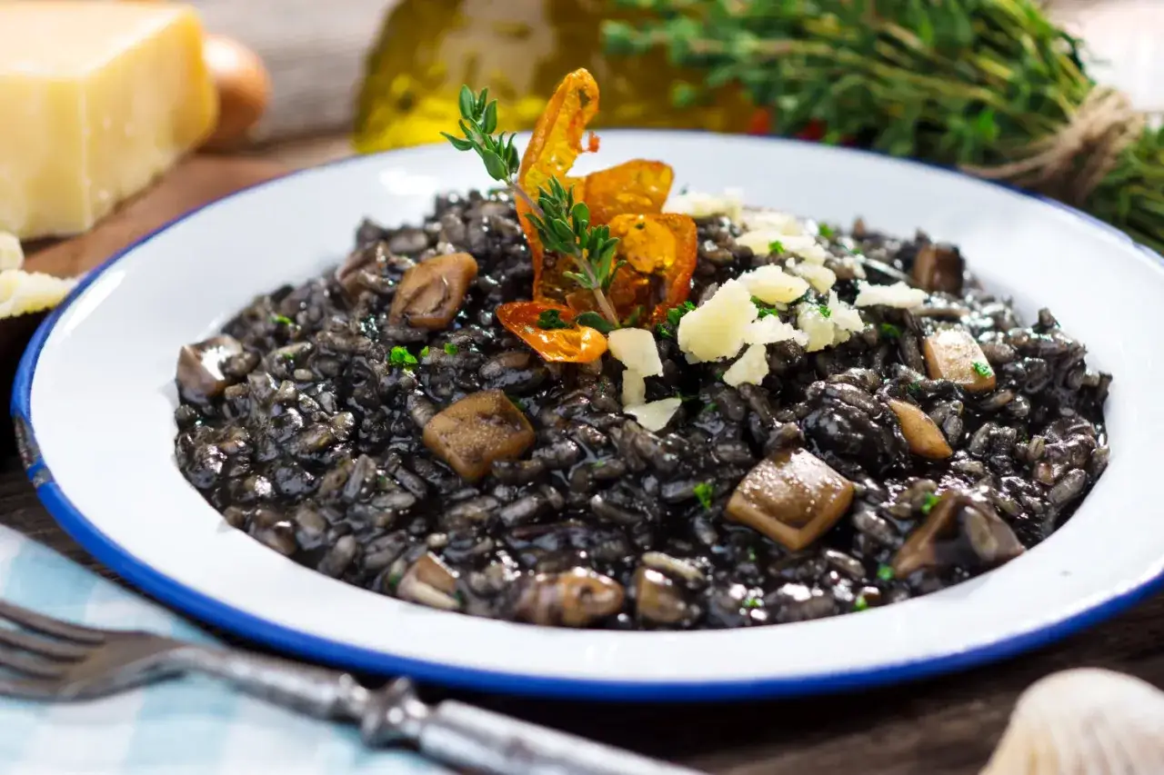 Risotto noir, à base d'encre de seiche c'est quoi ? Ce plat savoureux est garni de champignons et de copeaux de parmesan.