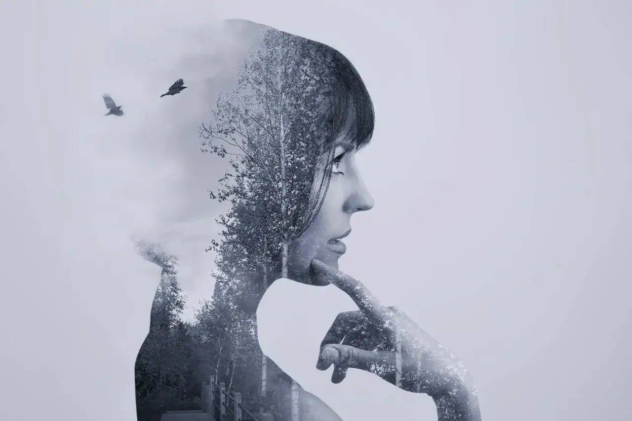 Silueta de mujer pensativa en **doble exposici&oacute;n**, con un bosque y dos cuervos volando integrados en su perfil.