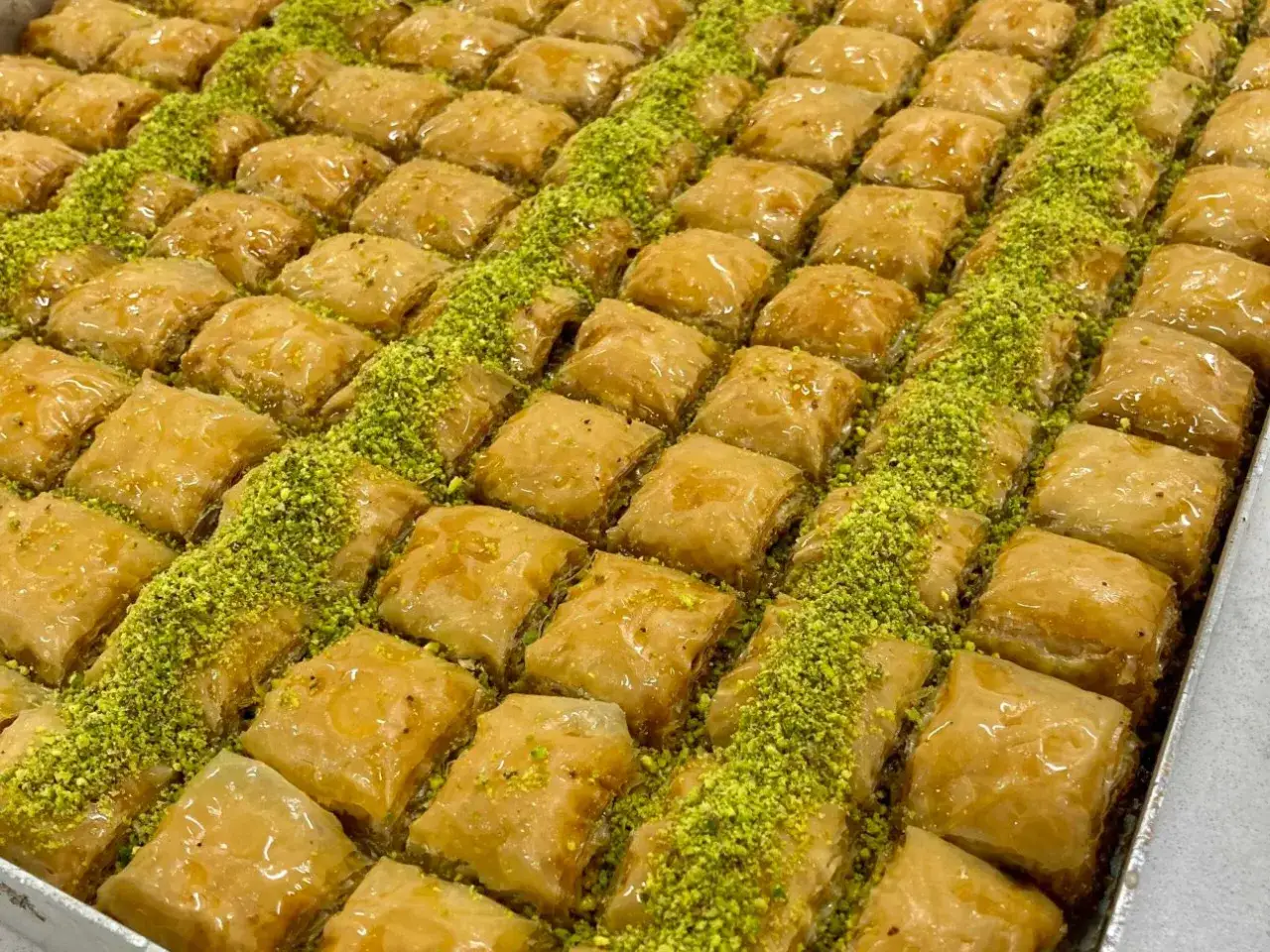 En stor bricka med gyllene, krispiga baklava-bitar, generöst strödda med gröna pistagenötter. Perfekt för ett baklava recept!