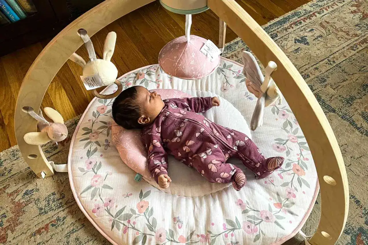 S&ouml;t bebis i en mjuk babygym med kant, omgiven av h&auml;ngande leksaker.