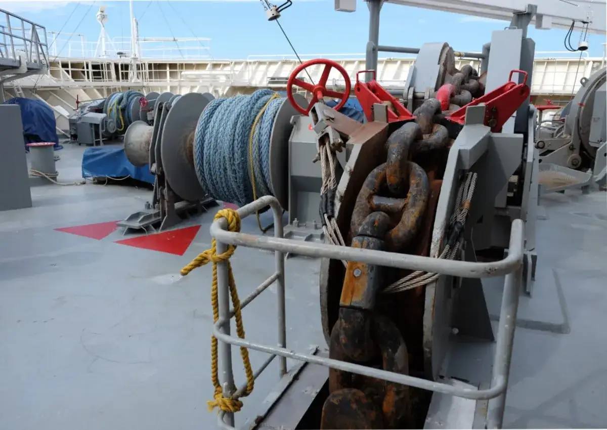 Gros plan sur l'ancre d'un paquebot, avec sa cha&icirc;ne rouill&eacute;e et un treuil enroul&eacute; de cordage bleu.