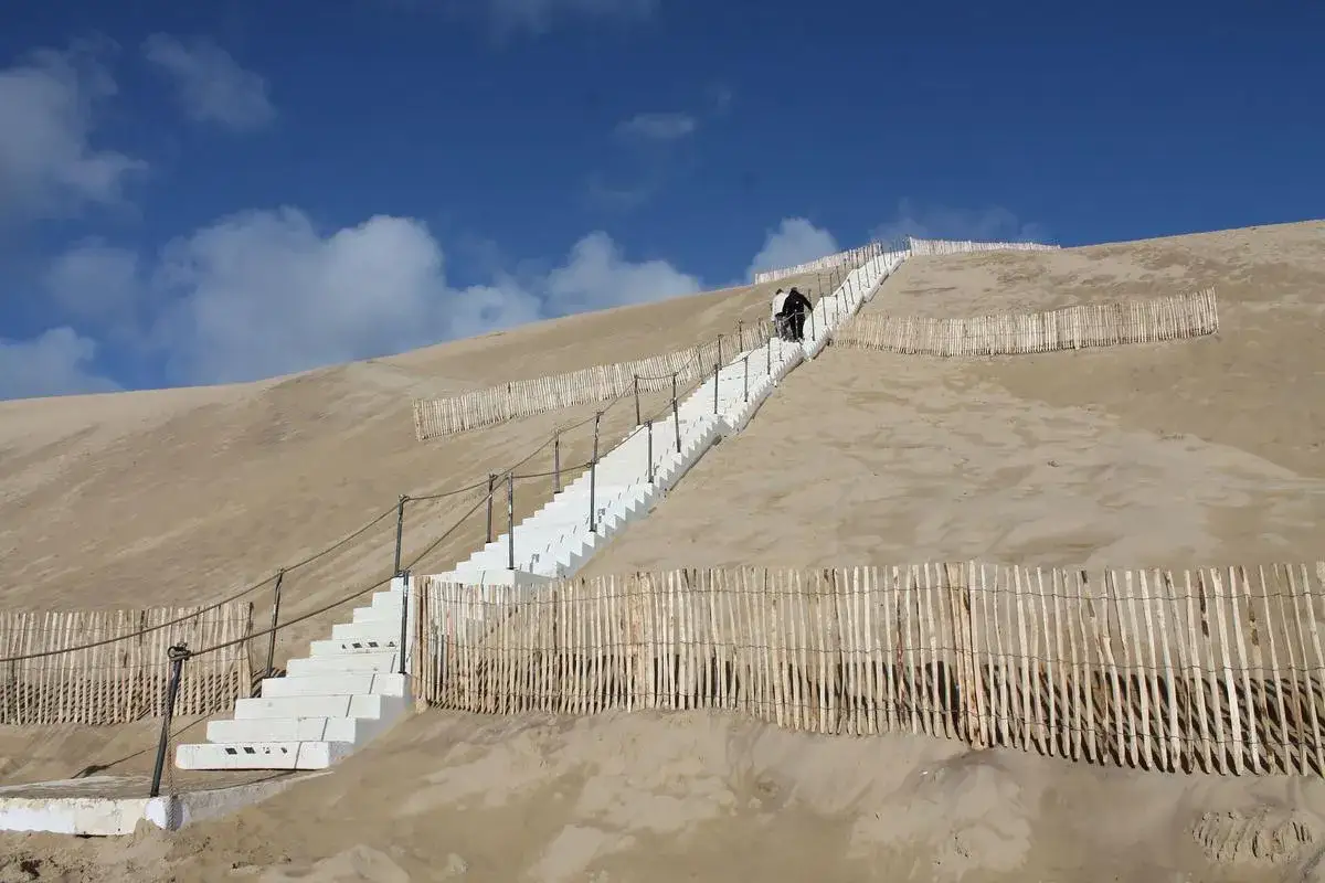 Escaliers blancs menant au sommet de la dune du Pilat, offrant un itin&eacute;raire spectaculaire. Des barri&egrave;res en bois prot&egrave;gent le sable.