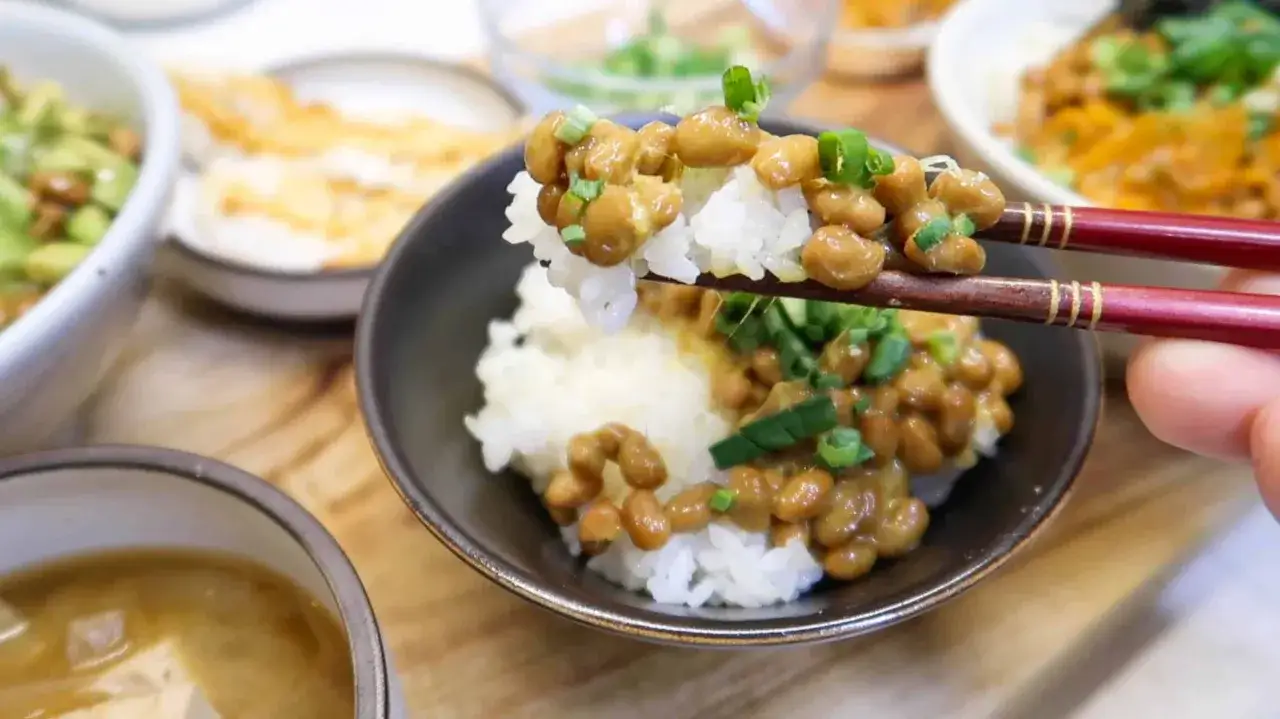 Pałeczki podnoszą ryż z kleistym, brązowym **natto**. Co to jest? Fermentowana soja z zieloną cebulką, podana w miseczce.