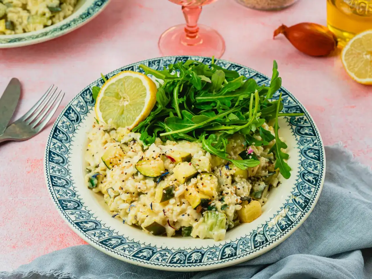 Un cr&eacute;meux risotto courgette, garni de roquette fra&icirc;che et d'une tranche de citron, sur une assiette orn&eacute;e.