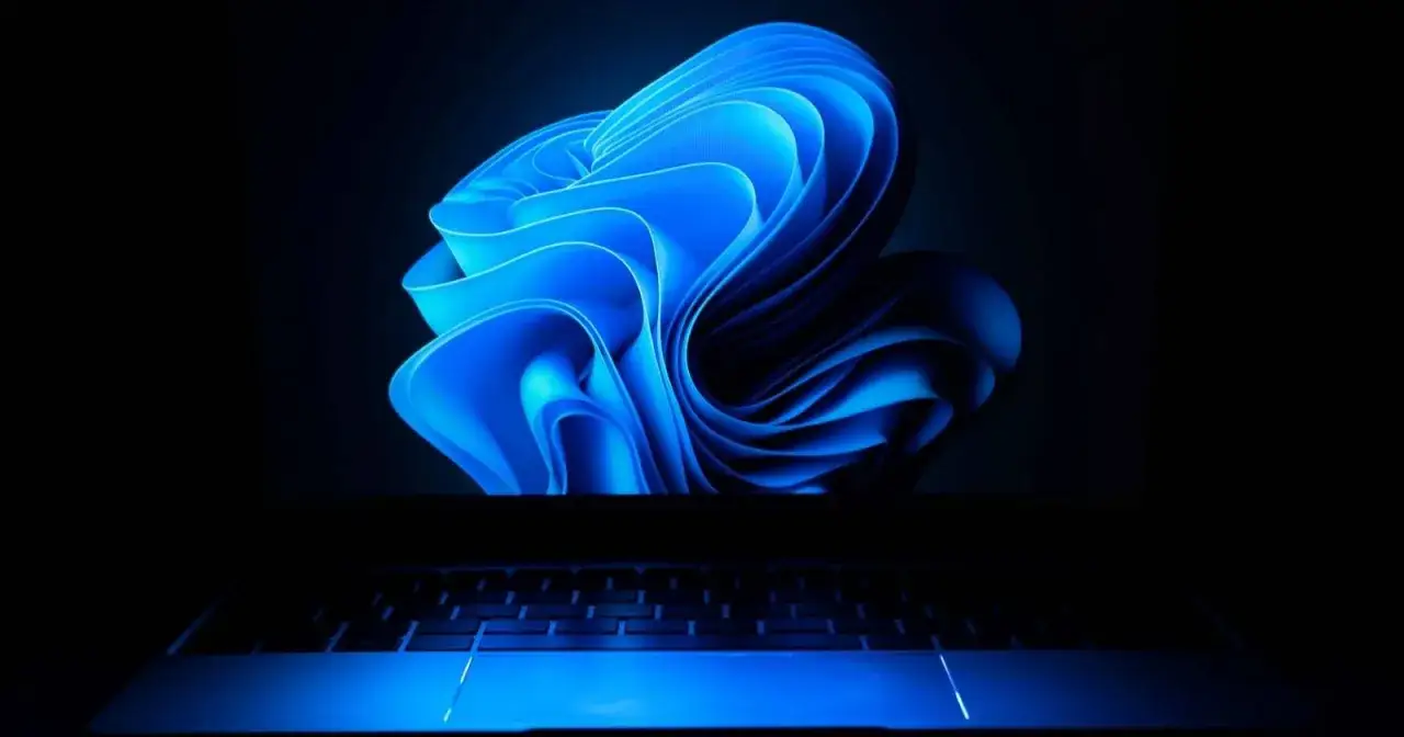 Niebieski, falujący wygaszacz ekranu Windows 11 na ciemnym tle, z podświetlaną klawiaturą laptopa.