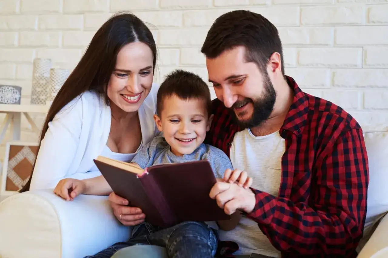 A happy family enjoys a moment of family bible study, gathered around a book on a couch.