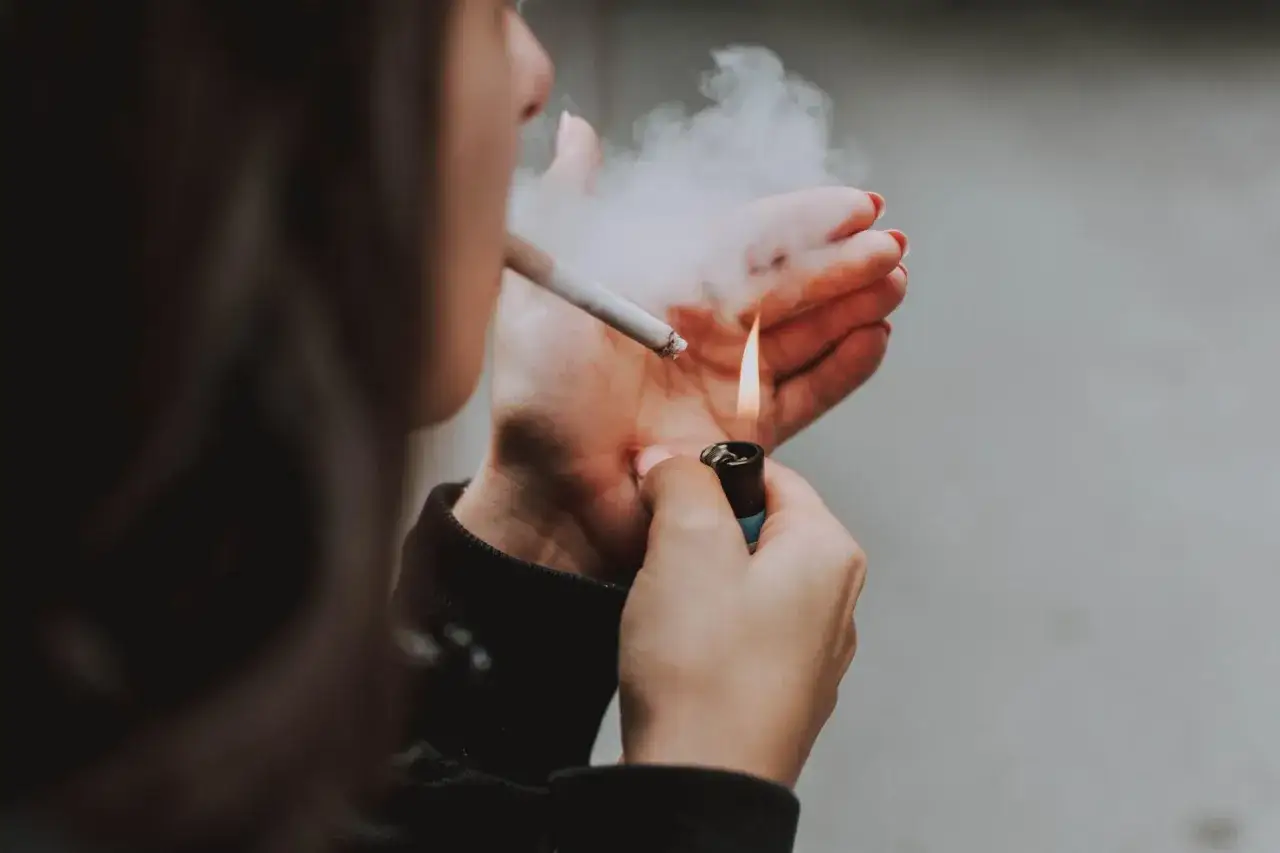 Dłoń z zapalniczką i papierosem, z którego unosi się dym. Kotynina w akcji.