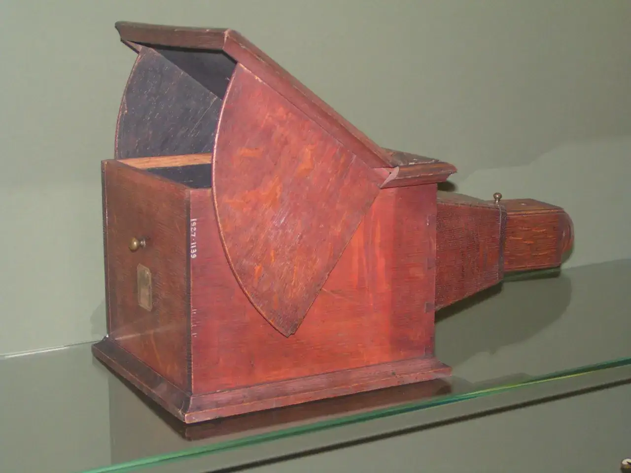Drewniana camera obscura z otworem i lustrem, stojąca na szklanej półce.