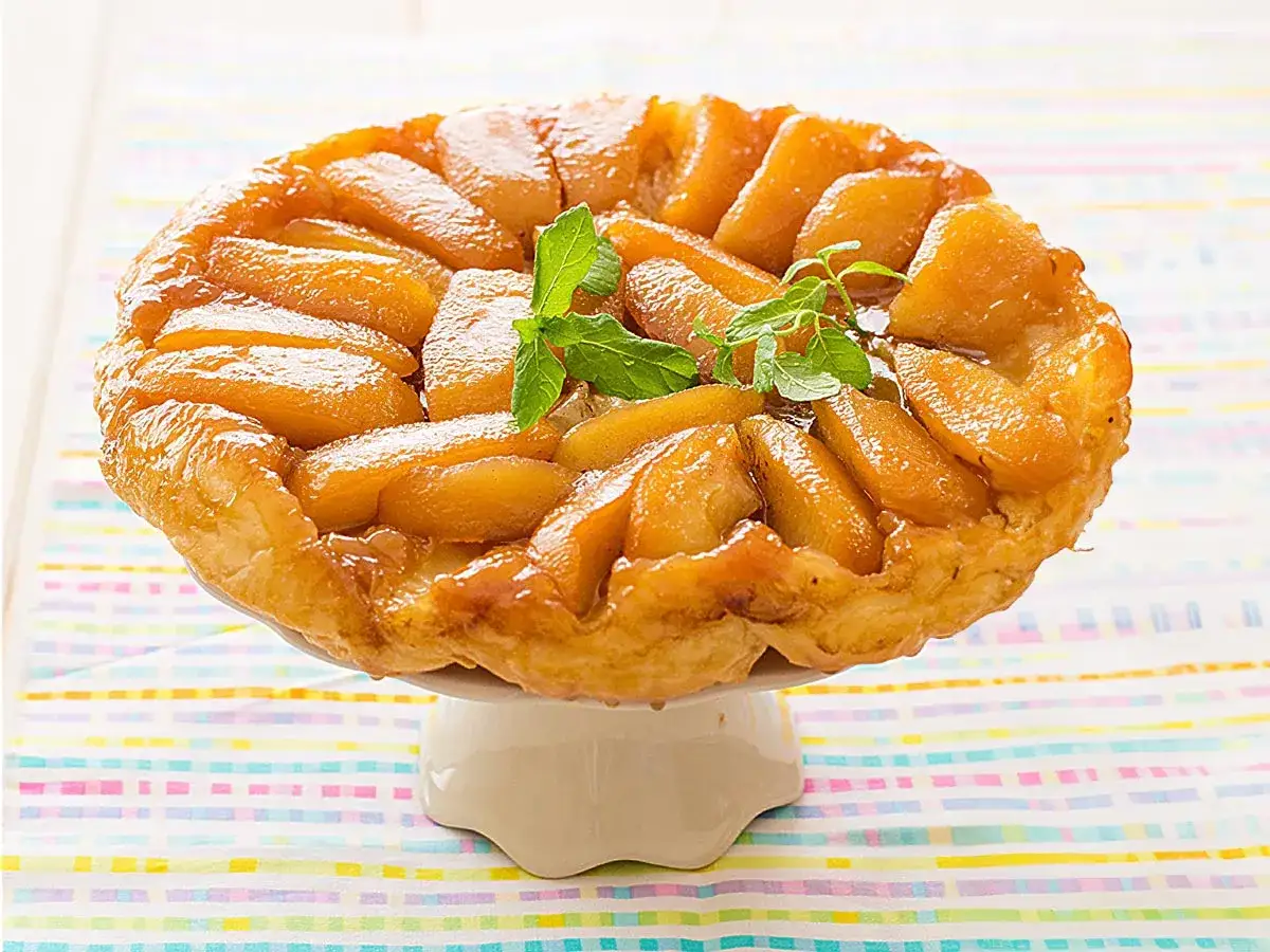 Delicioso tatin de manzana caramelizado, con trozos de manzana dorados y una masa hojaldrada crujiente, decorado con hojas de menta fresca.