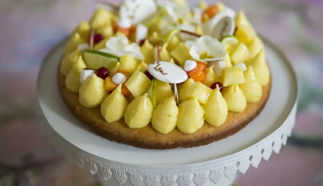 Deliziosa torta Raffaello con crema gialla, frutta esotica e meringhe su un'alzata bianca.