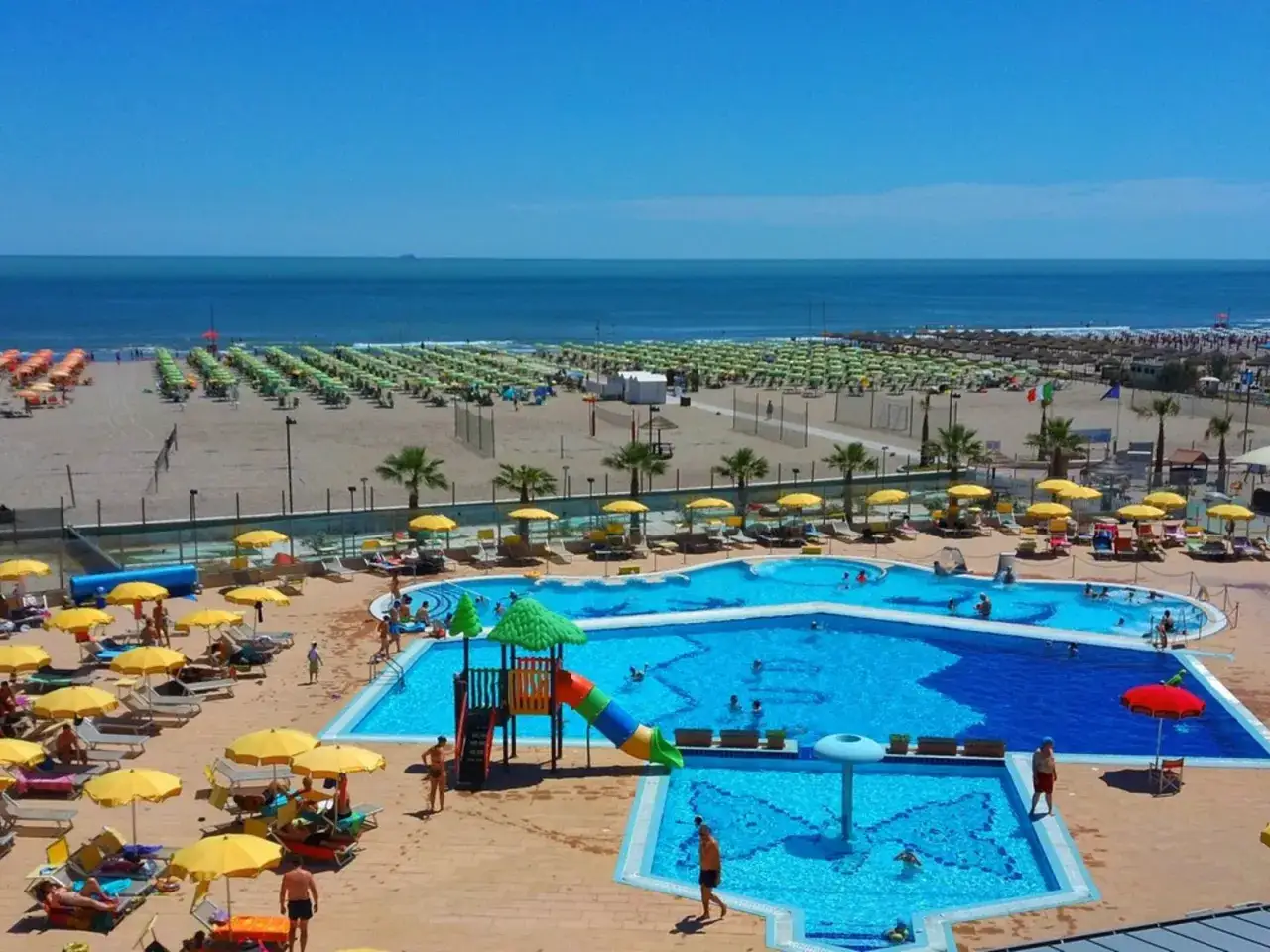 Sonnige Tage am Strand von Rosapineta Sud. Ein Pool mit Rutsche l&auml;dt zum Planschen ein, w&auml;hrend am Meer Liegen und Sonnenschirme auf Besucher warten.