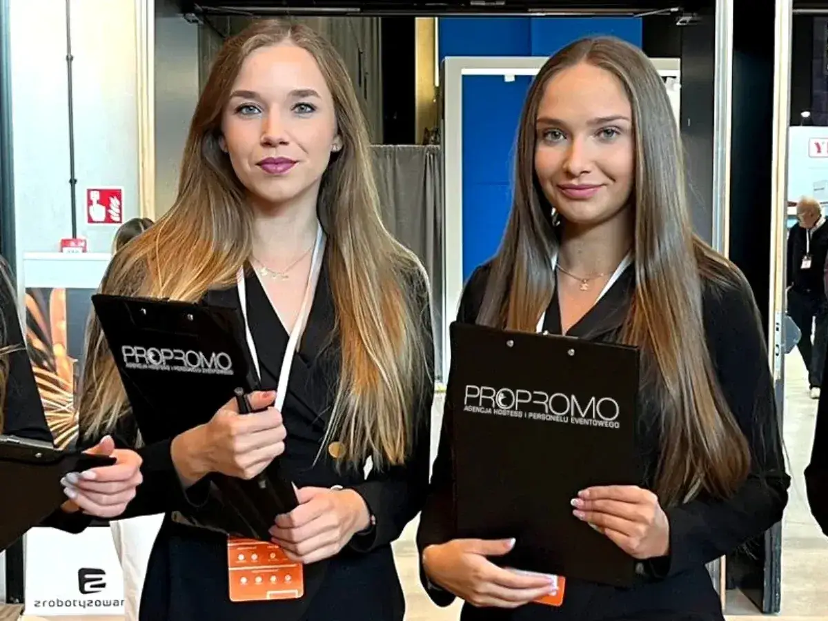 Dwie uśmiechnięte hostessa z agencji PROPROMO trzymają teczki z logo firmy.