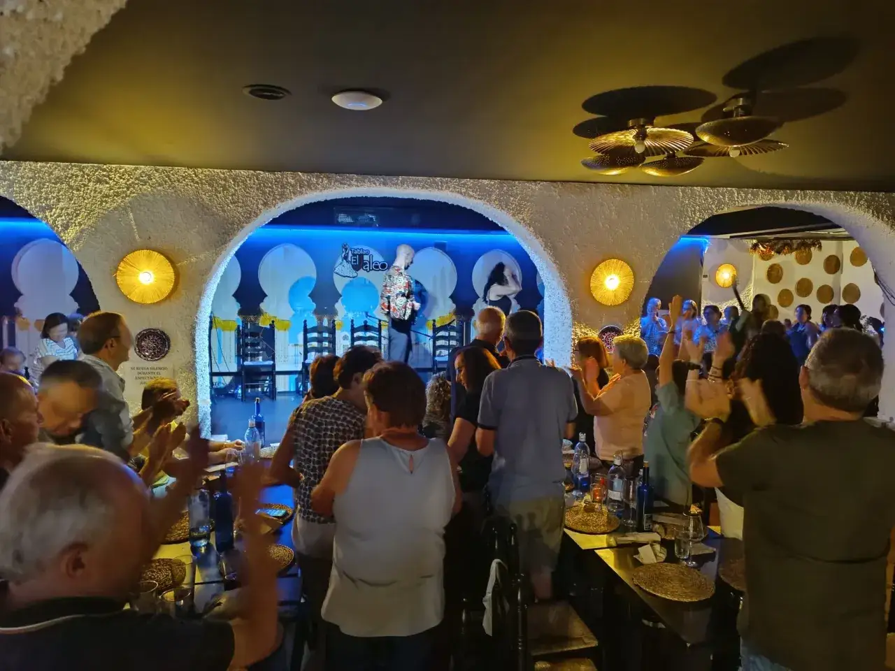 Un público aplaude con entusiasmo en un tablao flamenco. El artista en el escenario recibe un