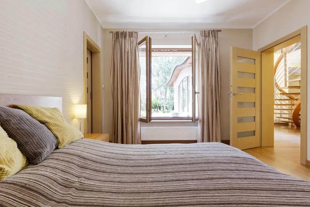 Letto a righe con cuscini, finestra aperta su un giardino lussureggiante e una scala a chiocciola visibile attraverso una porta. Forse &egrave; per questo che non aprire le finestre di notte.