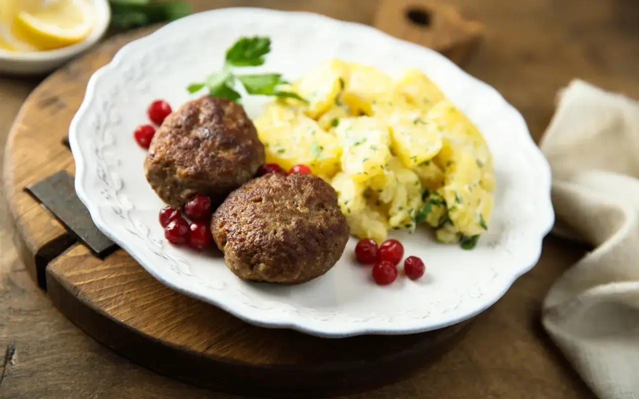 Zwei saftige Fleischpflanzerl mit Kartoffelsalat und Preiselbeeren. Ein leckeres Fleischpflanzerl Rezept für Genießer.