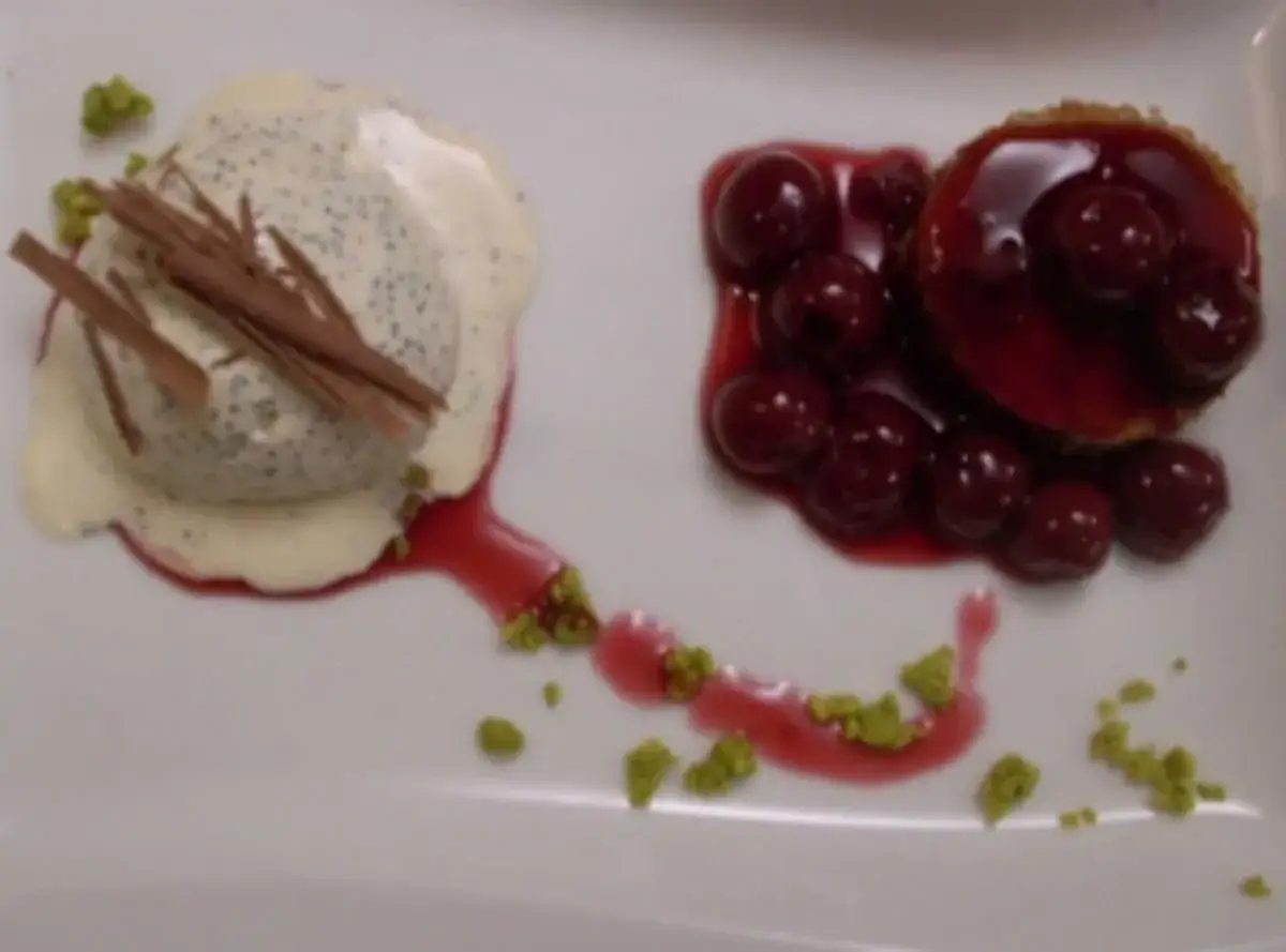 Ein cremiges Mohn Eis mit Schokoladenraspeln und Kirschen auf einem weißen Teller.