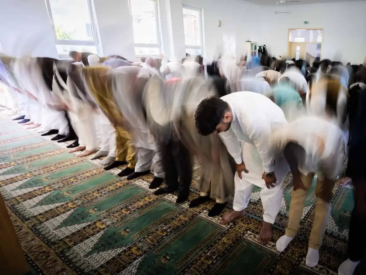 M&auml;nner beugen sich im Gebet in einer Moschee, ein bewegtes Bild, das die Gemeinschaft w&auml;hrend des Eid al-Adha zeigt.
