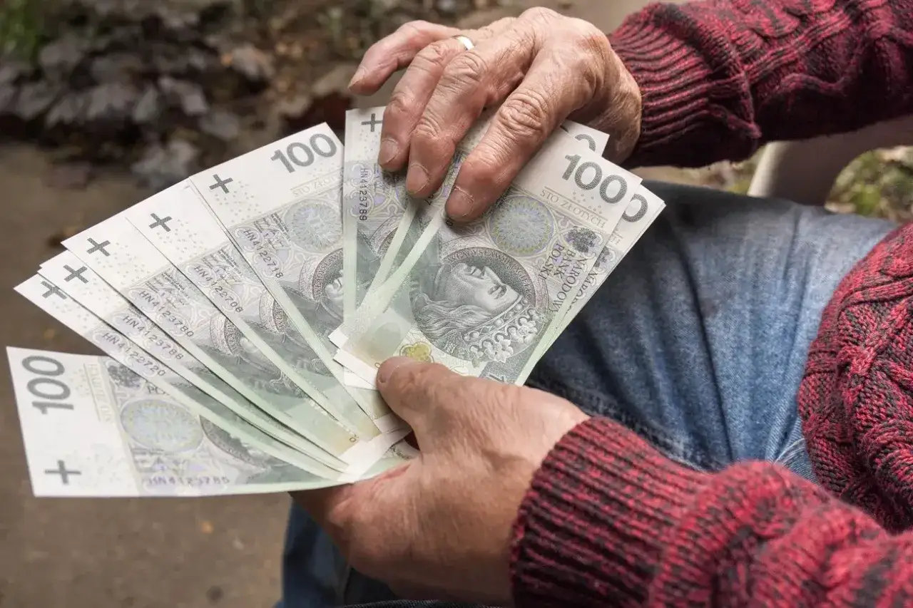 Dłoń trzyma plik banknotów 100 zł. Czy to wystarczy na leczenie po zawał serca i jaka grupą inwalidzką po zawale serca?