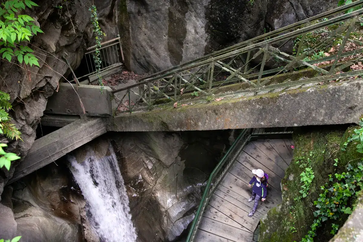 Bambina esplora l'orrido di Bellano, scendendo una scalinata di legno accanto a una cascata.