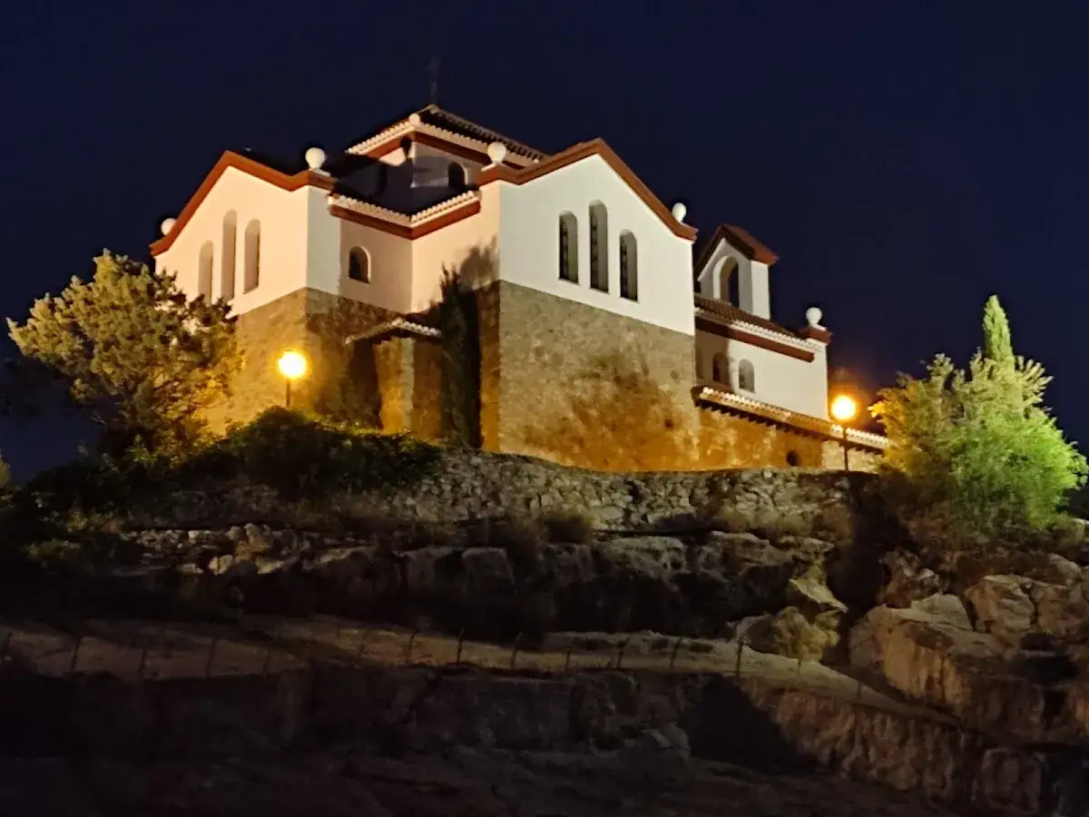 La ermita de los Tres Juanes, iluminada por farolas, se alza sobre una colina rocosa bajo el cielo nocturno.