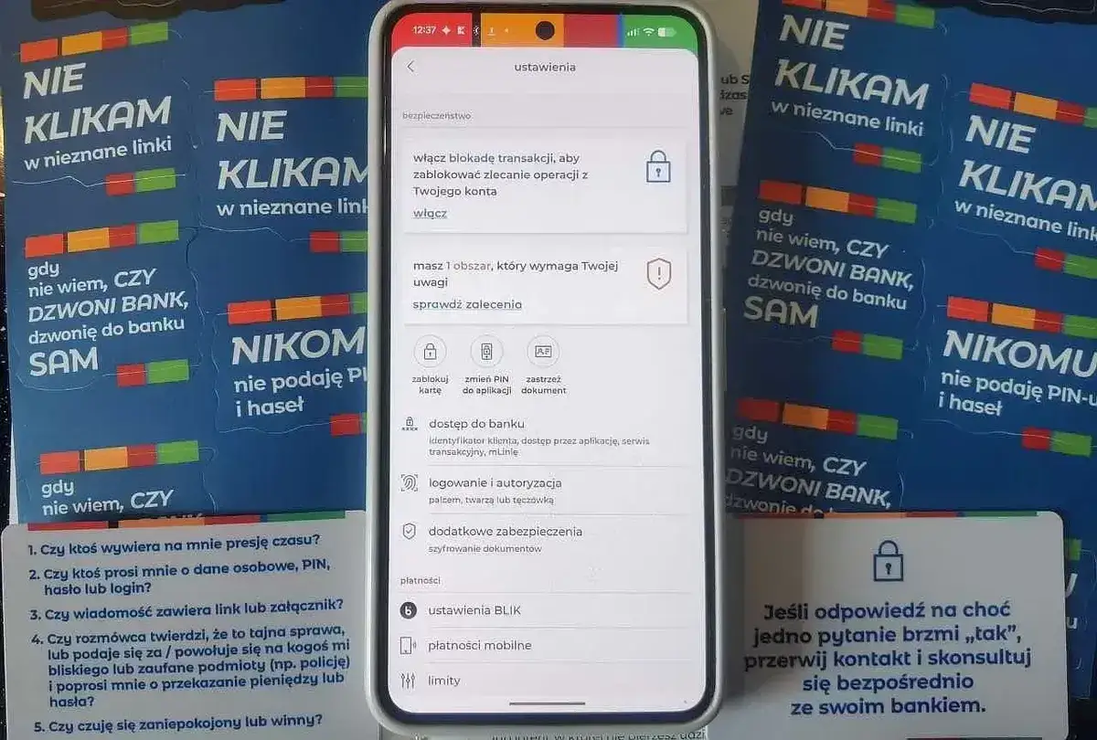 Aplikacja bankowa na telefonie pokazuje ustawienia bezpieczeństwa, a obok ulotki ostrzegają przed oszustwami. Czy Revolut jest bezpieczny? Sprawdź ustawienia i bądź ostrożny.