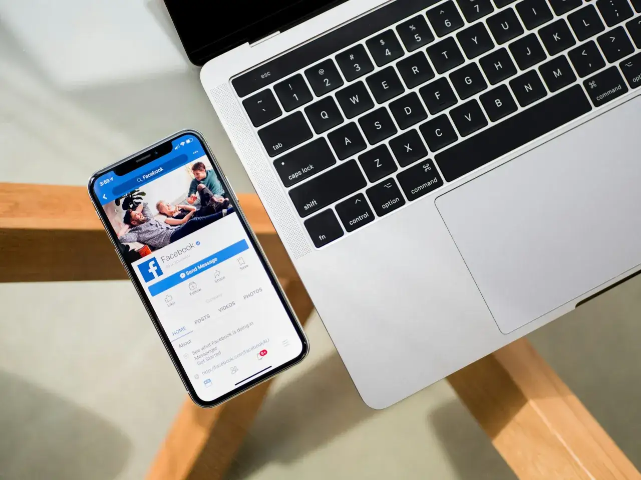 Telefon z Facebookiem obok laptopa. Dowiedz się, jak wylogować się z fb na innych urządzeniach, by zapewnić bezpieczeństwo.
