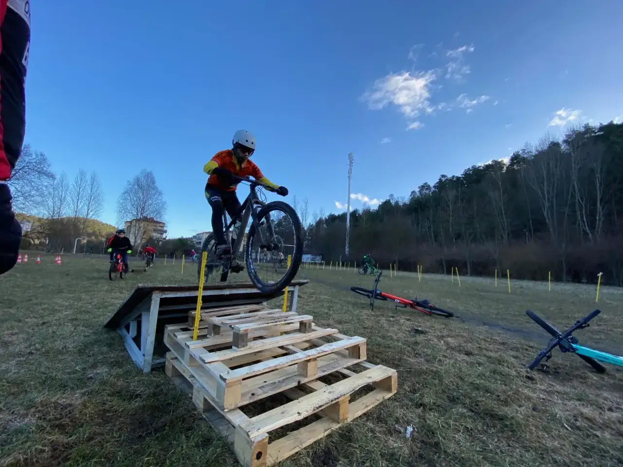 Młody kolarz w kasku pokonuje przeszkodę z palet podczas zawod&oacute;w MTB.