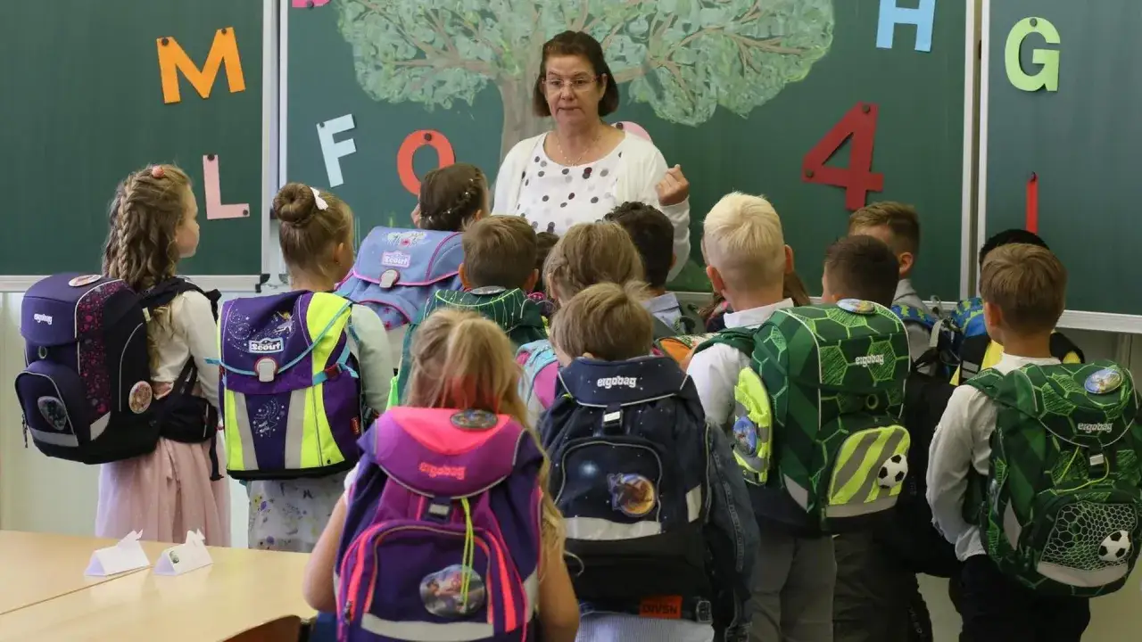 Lehrerin erkl&auml;rt Kindern mit Schulranzen im Unterricht. Die **Ganztagsbetreuung Grundschule** beginnt mit spannenden Lektionen.
