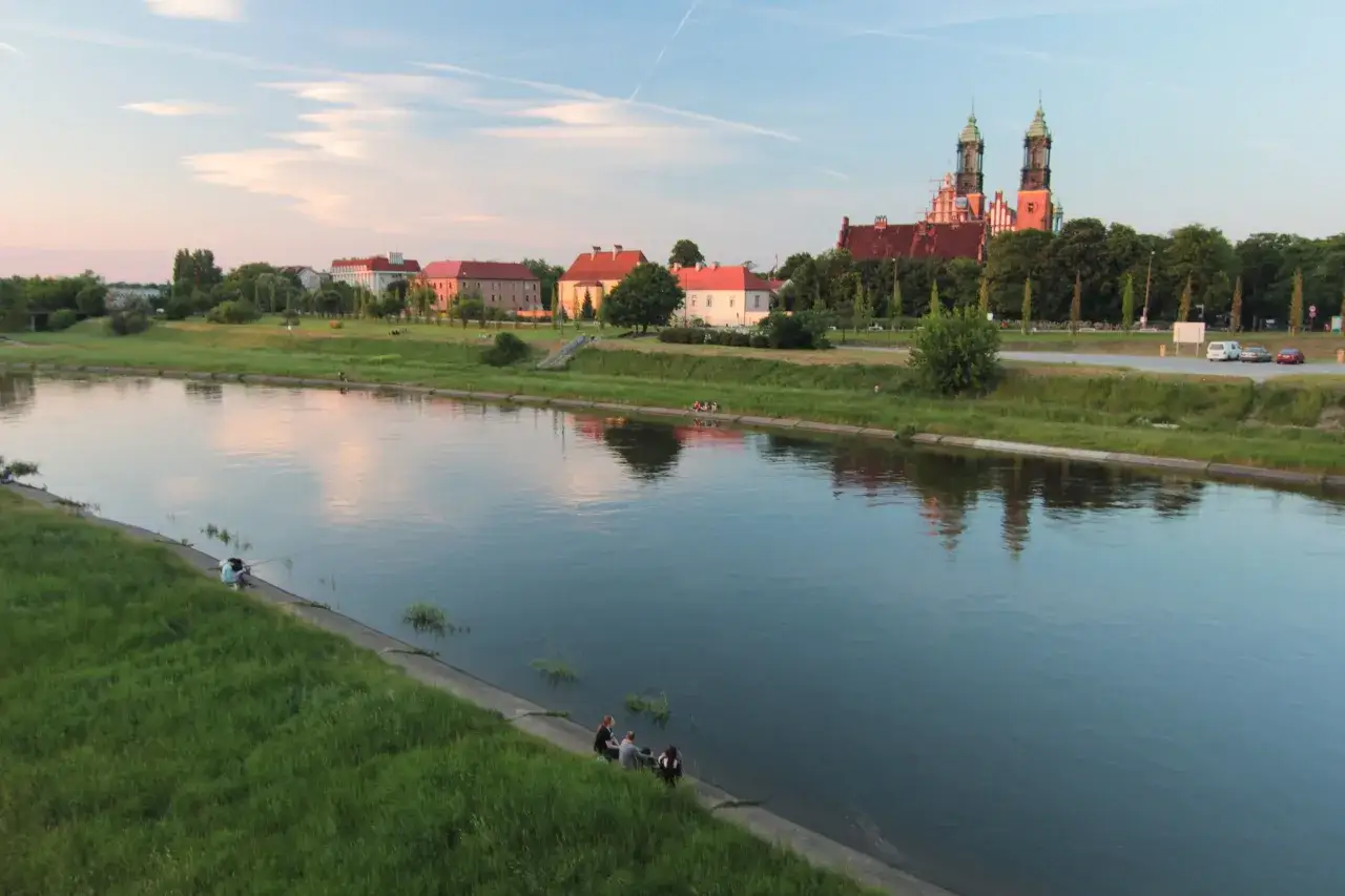 Zach&oacute;d słońca nad Wartą, z widokiem na poznańskie atrakcje: katedrę i nadbrzeże.