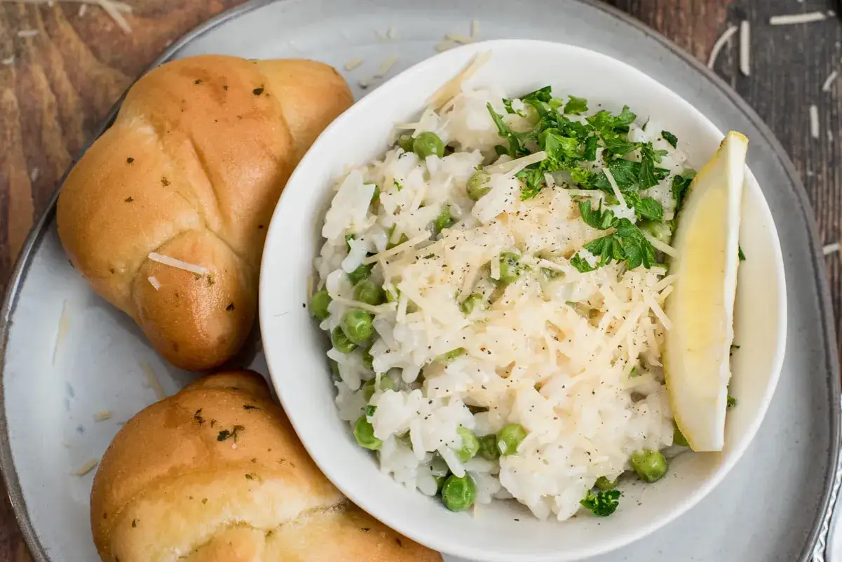 Pyszne risotto cytrynowe z groszkiem, posypane parmezanem i natką pietruszki, podane z bułeczkami.