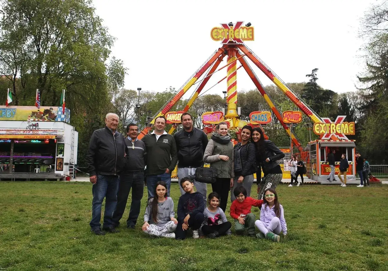 Famiglie giostrai italiani posano sorridenti davanti a un'attrazione da luna park.